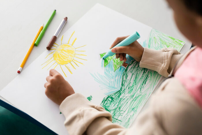 Child drawing a landscape with markers.