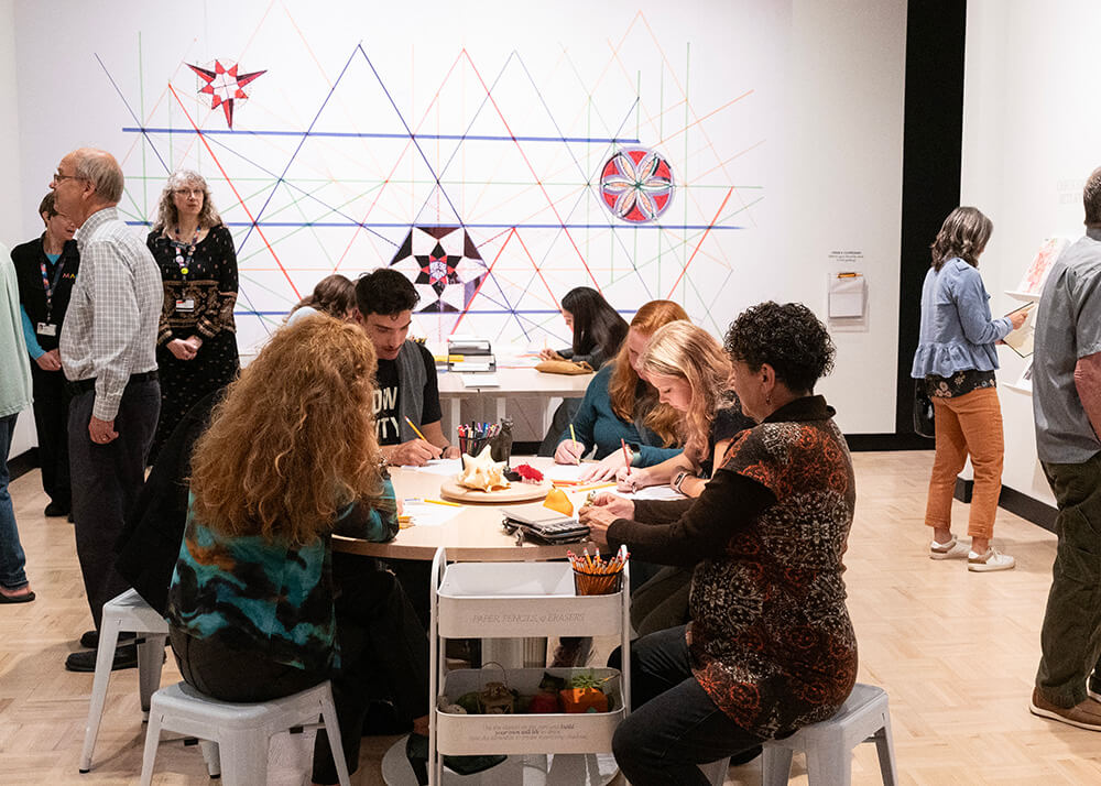 A crowd of people, both seated and standing, in the drawing lab that's part of the Drawing as Discovery exhibition.