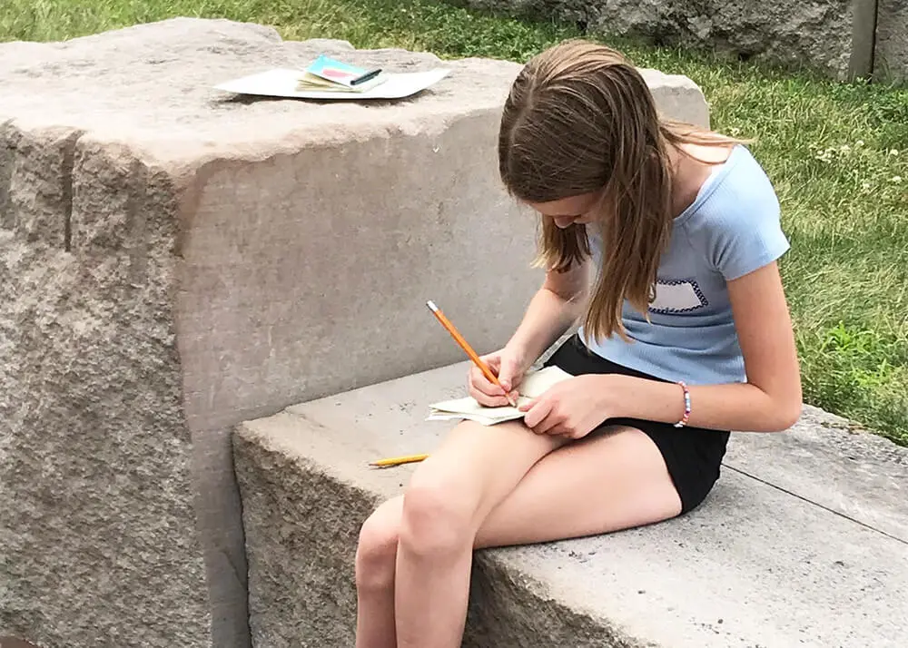 A girl drawing in a sketchbook outside.