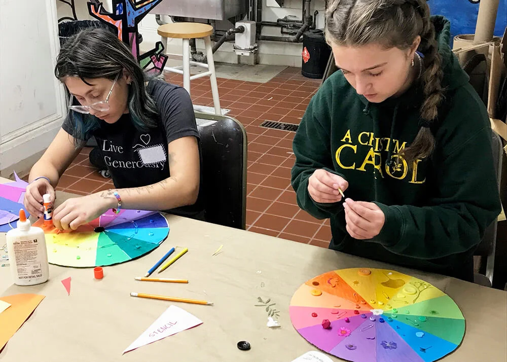 Two girls creating painted and collaged color wheels.