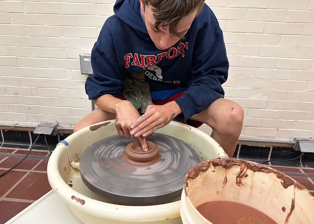 A boy throwing a ceramic pot on a potter's wheel.