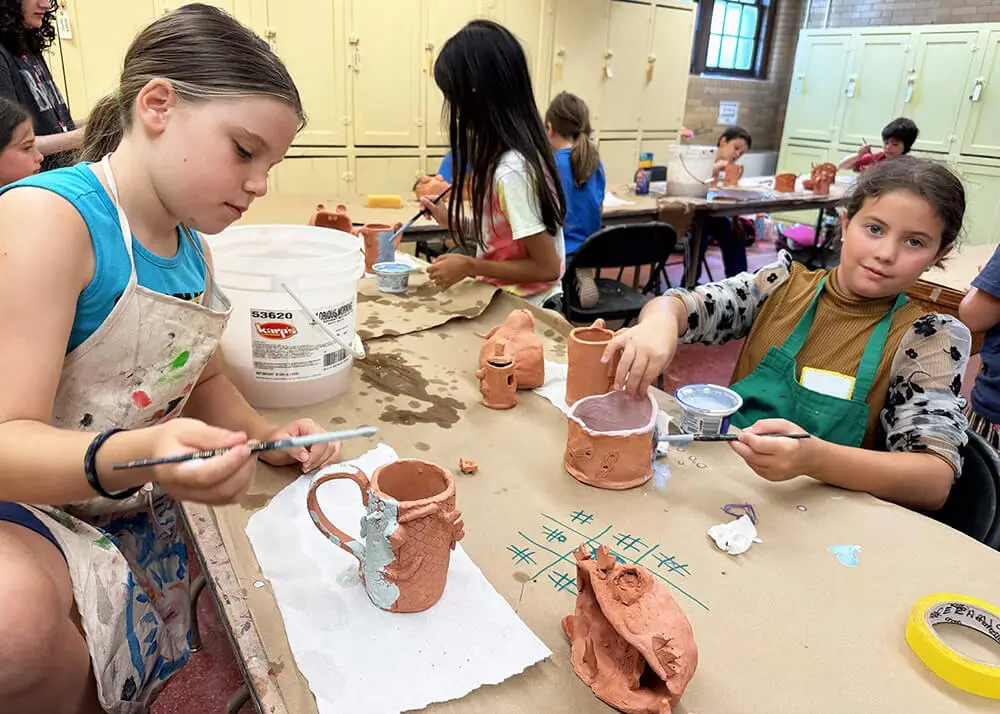 Two kids glazing handmade ceramic mugs.