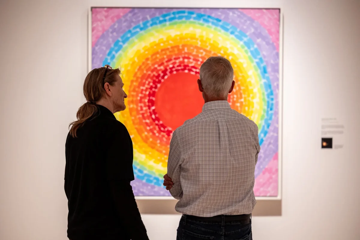 Two visitors looking at a brilliant painting in the exhibition Composing Color: Paintings by Alma Thomas.