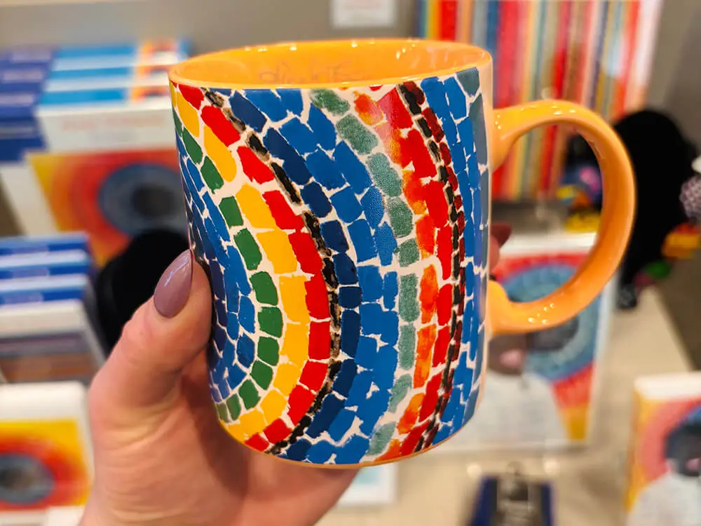 A coffee mug with colorful artwork by Alma Thomas on the side.