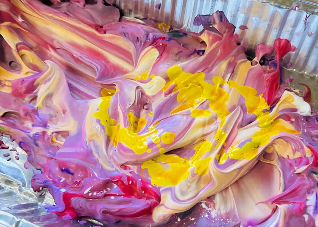 Colorful swirls of paint mixing in a tin.