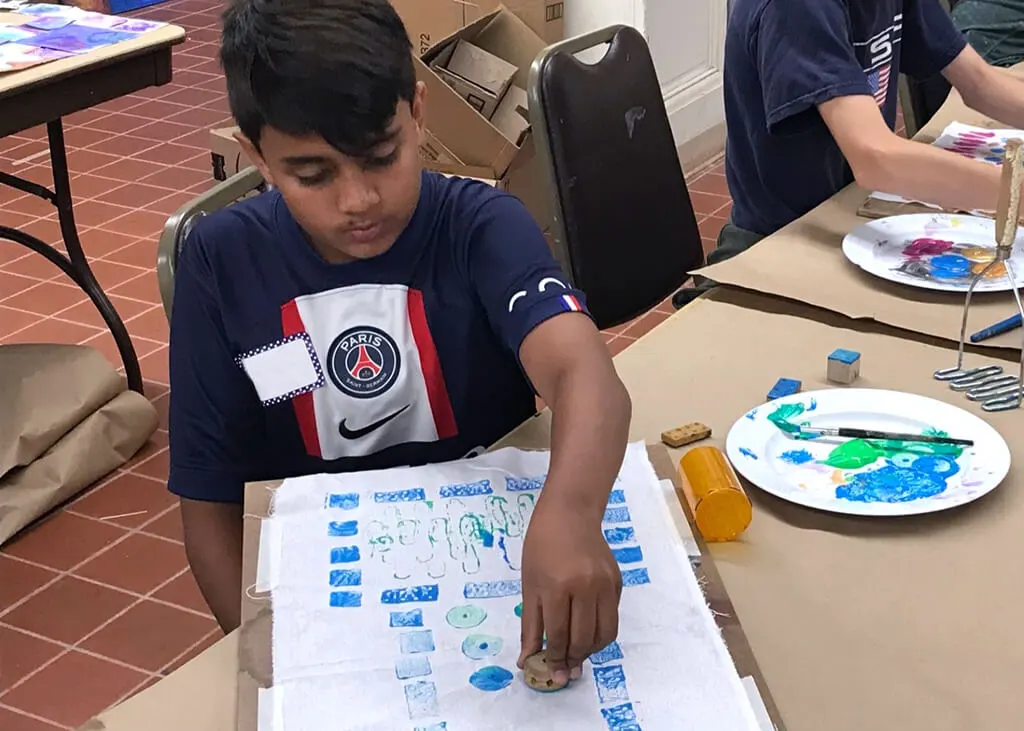 A boy stamping designs on fabric with paint.