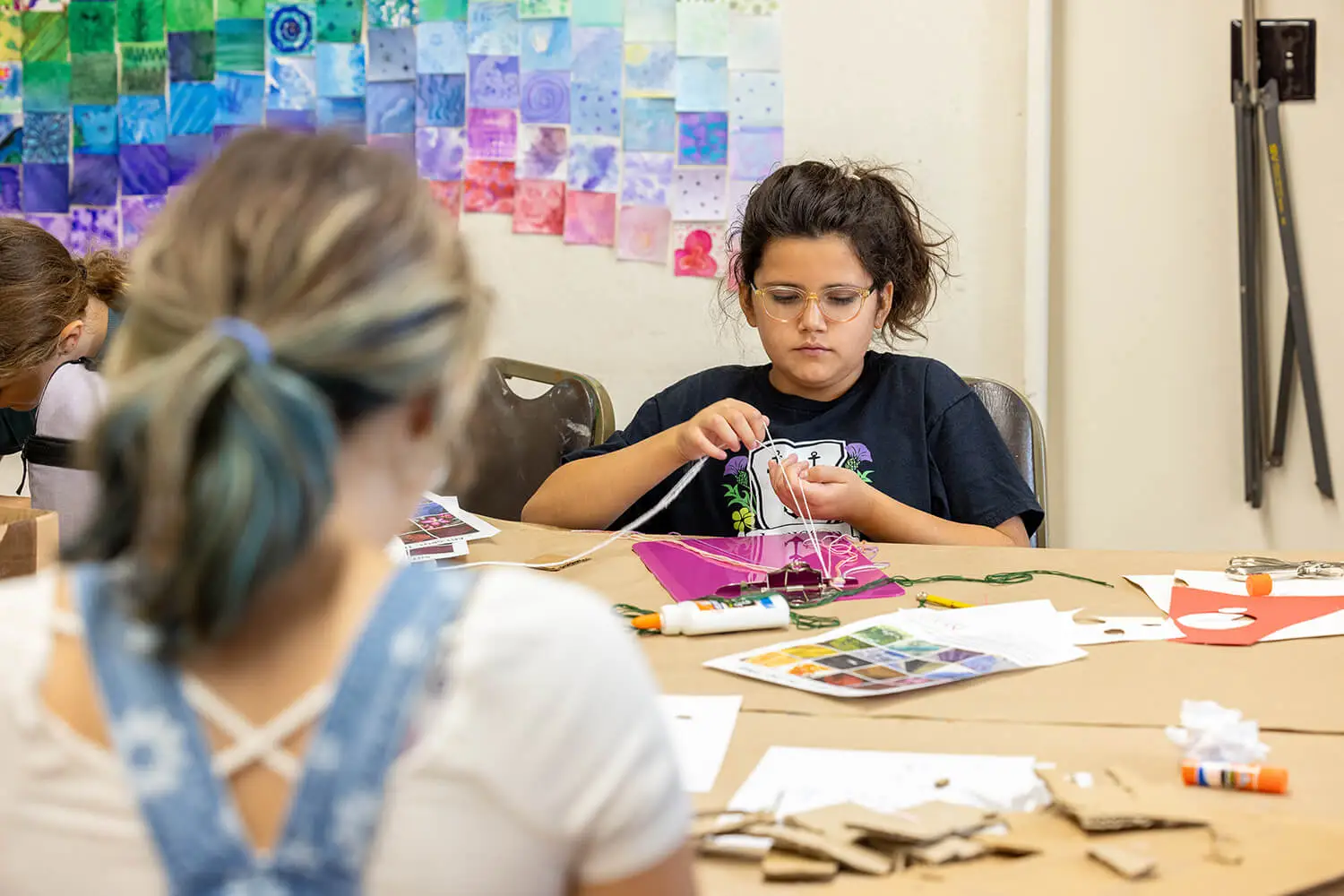 A girl braiding a rainbow bracelet with other kids in the Creative Workshop.