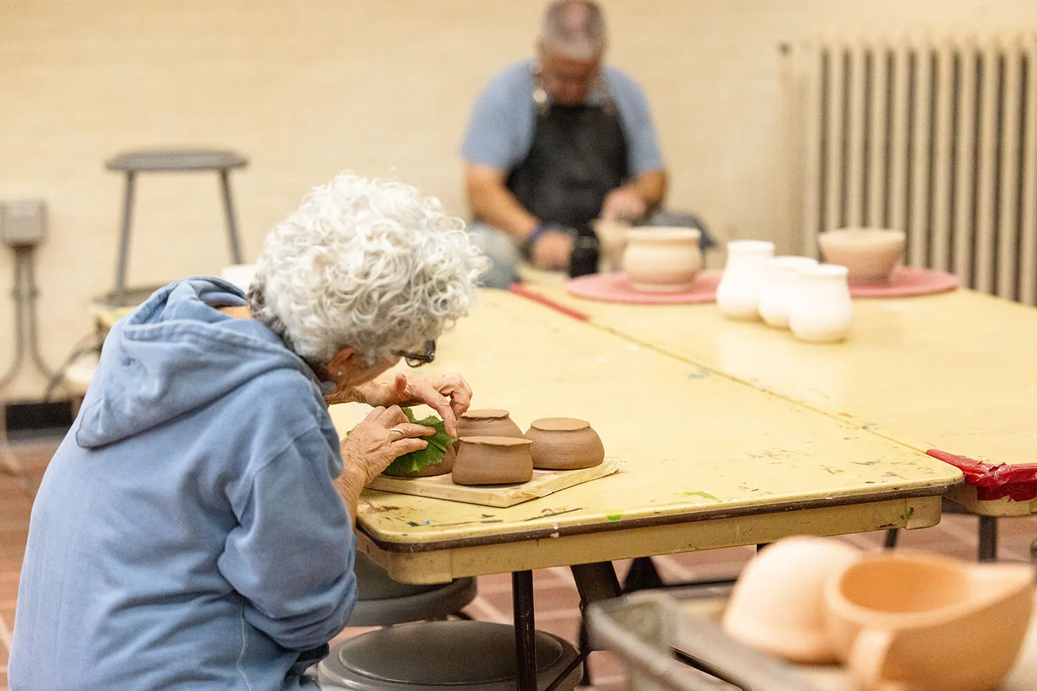 A person carefully pressing a leaf to ceramic pots to leave impressions on them.