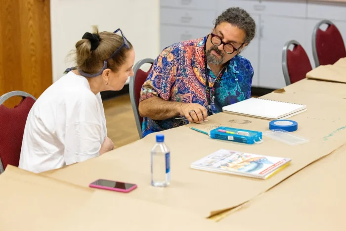 A teacher sketching on craft paper to demonstrate a technique to a student.