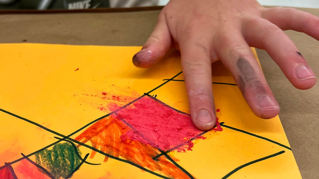 A kid's fingers smudging red chalk on a drawing.