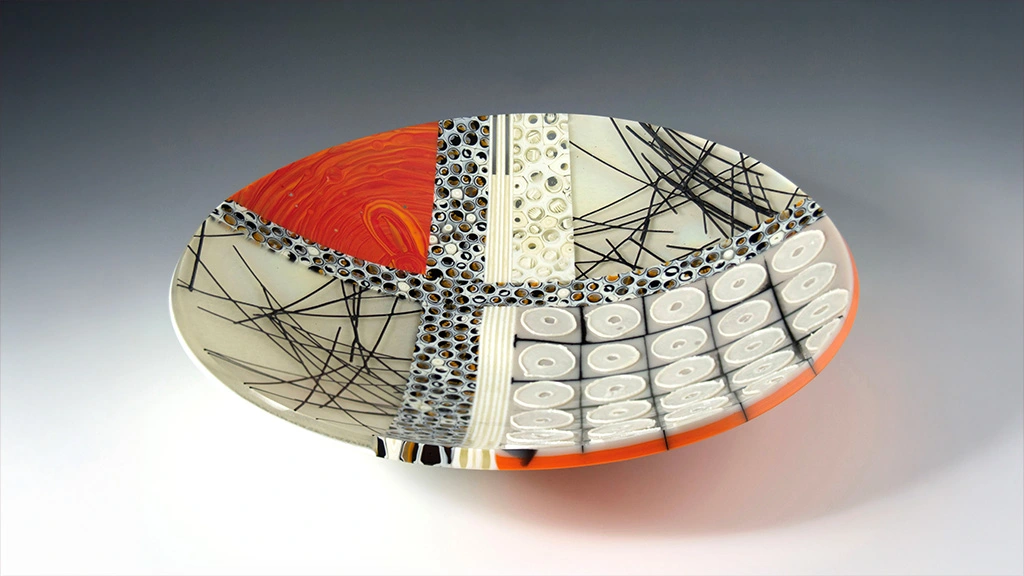A handmade glass plate decorated with various patterns in cream, red, and black.