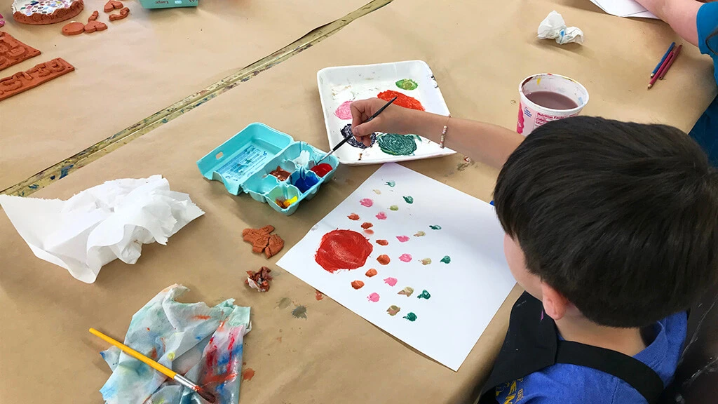A boy works on a colorful painting in the Creative Workshop.