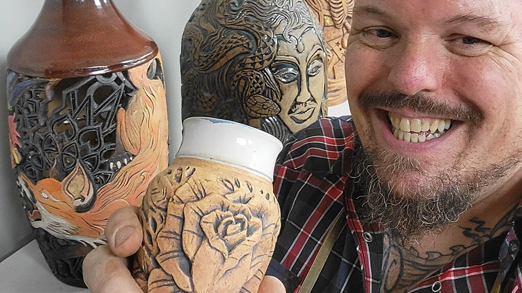 Instructor Jason Ferguson smiling and holding a small ceramic vessel carved with a flower.