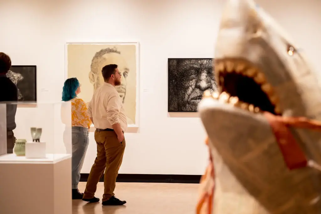 Two visitors wandering through the 69th Rochester-Finger Lakes Exhibition, a shark sculpture in the foreground.