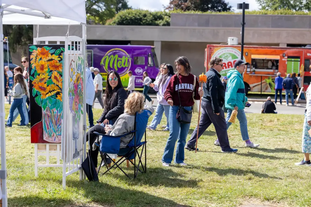Visitors walking through artist booths at Clothesline Art Festival, food trucks in the background.
