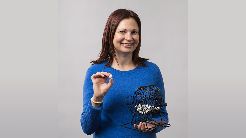 A woman holding up a bingo ball and smiling.