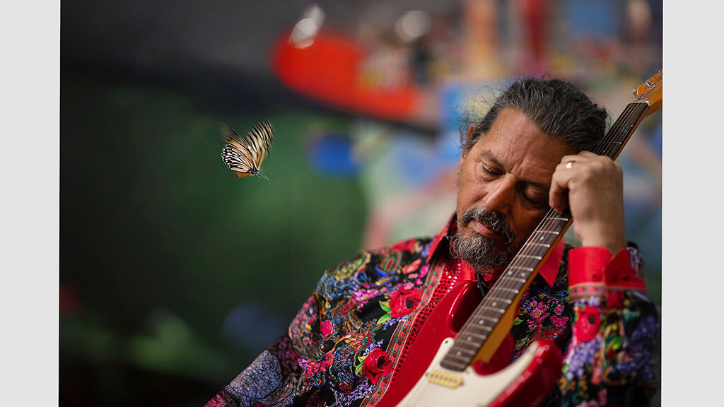 A man leaning his head against the neck of an electric guitar, seemingly asleep.