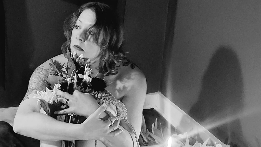A woman in greyscale, clutching a bouquet of flowers to her chest, looking mournfully to one side.