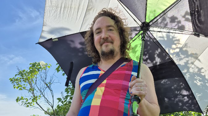 A man in a plaid tunic holding an umbrella on a sunny day.
