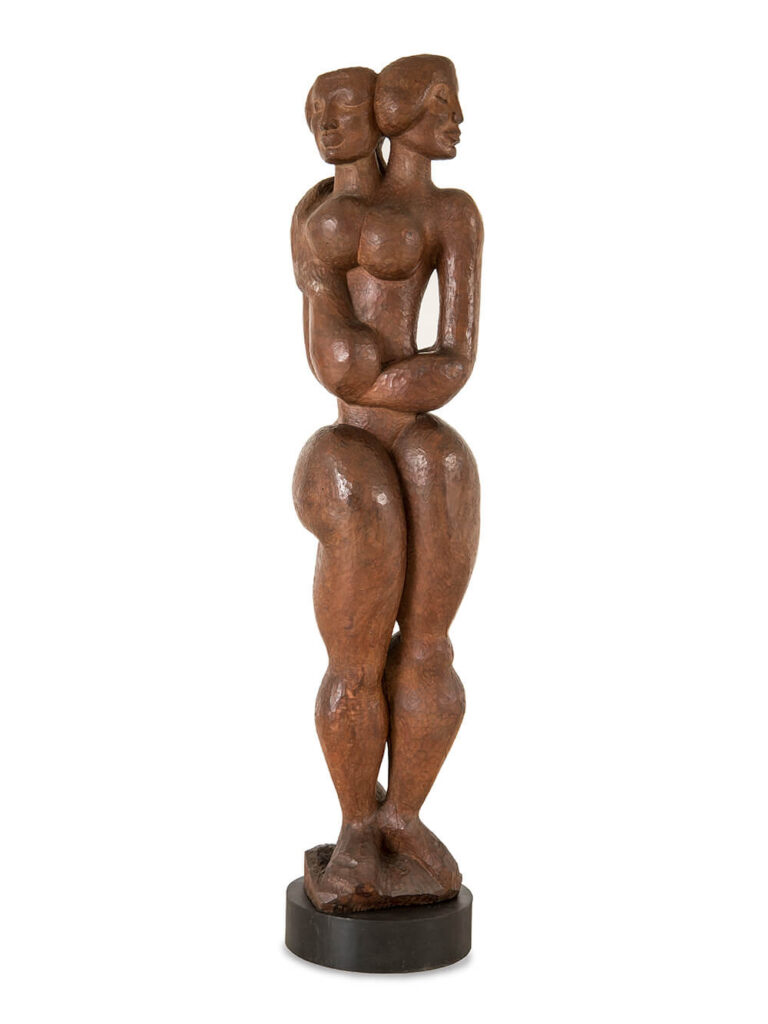 A wooden statue of two women embracing, their bodies merging into one form.
