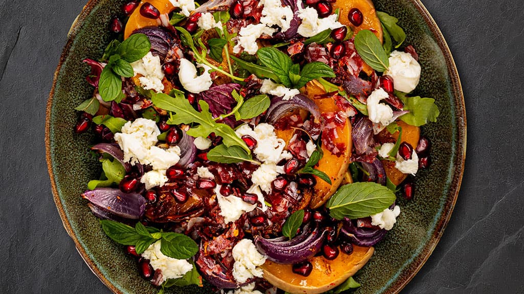 A close-up on a bowl of salad with fruits and fresh greens.