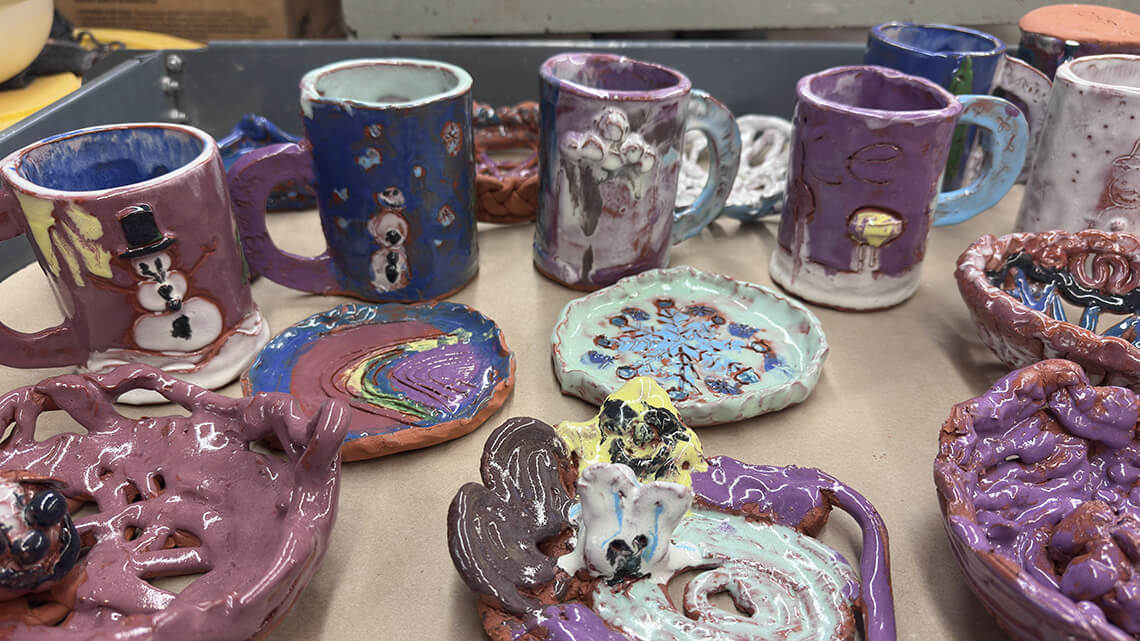 A table full of handmade mugs and plates, decorated in colorful glazes.