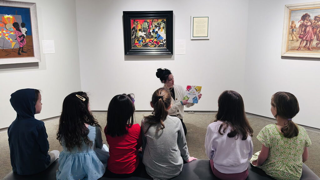 A Creative Workshop teacher reading a book on colors to a class of children in front of a colorful work of art in the galleries.