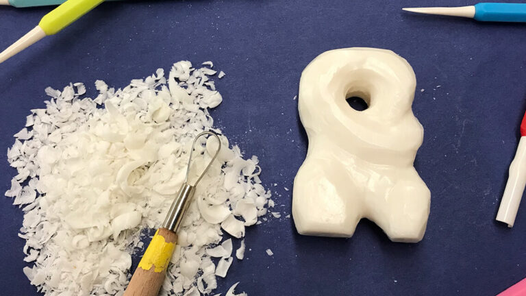 A carving in ivory soap, surrounded by carving tools and sitting next to a pile of soap shavings.