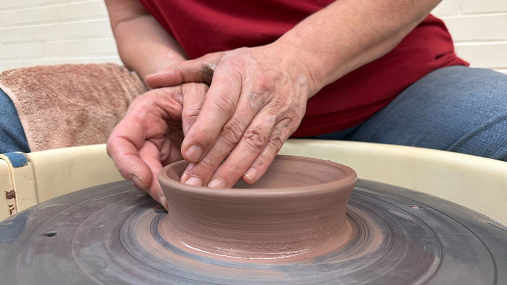 Hands carefully raising the side of a ceramic pot on the potter's wheel.
