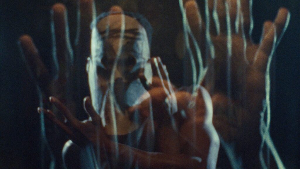 A person in a mask, overlaid with echoes of hands moving.