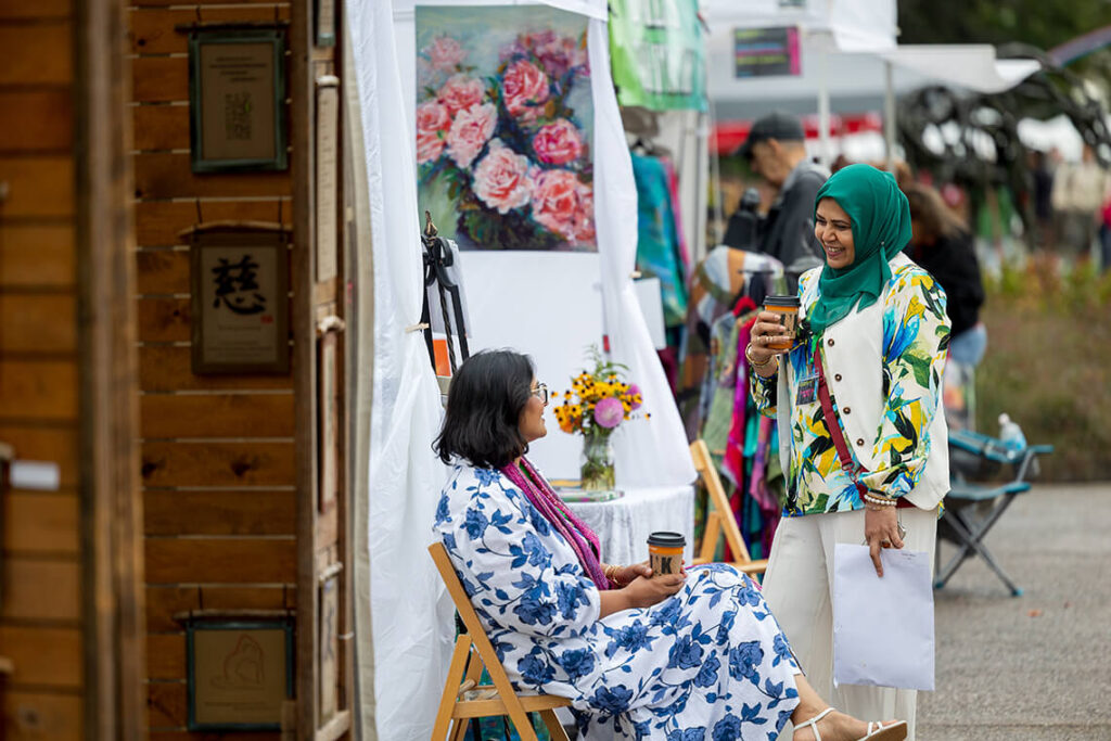 Two women talk next to an artist's booth at Clothesline.