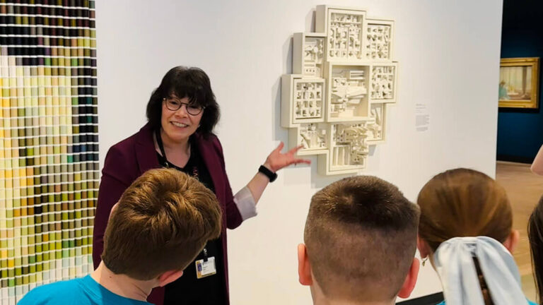 A woman discusses abstract artworks with a group of students in a museum.