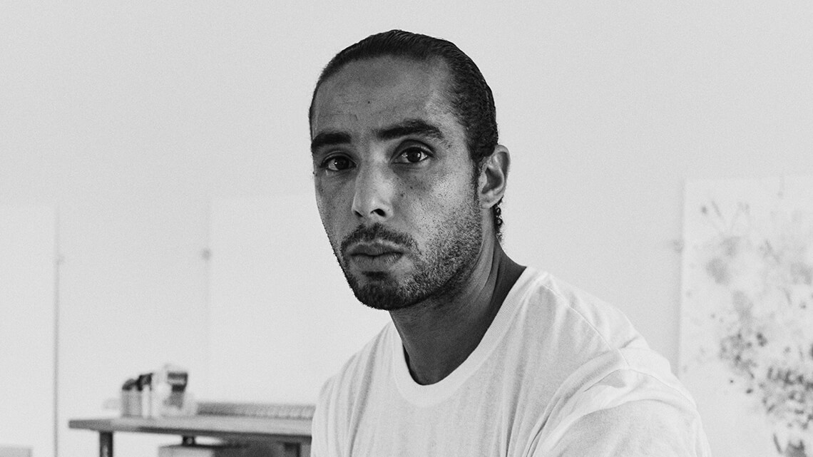 Hugo McCloud sitting casually in his studio, photographed in black and white.