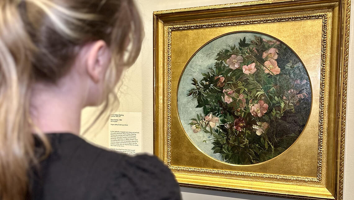 A woman looking at a floral still life in MAG's galleries.