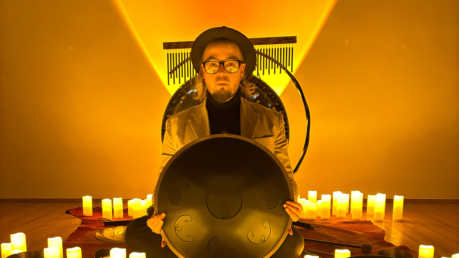 Harold Taddy holding a gong, sitting on a stage surrounded by candles.