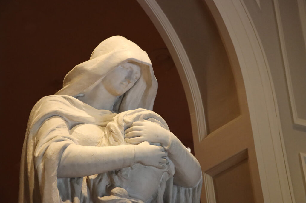 A marble statue of a woman looking mournfully down at an urn in her arms.