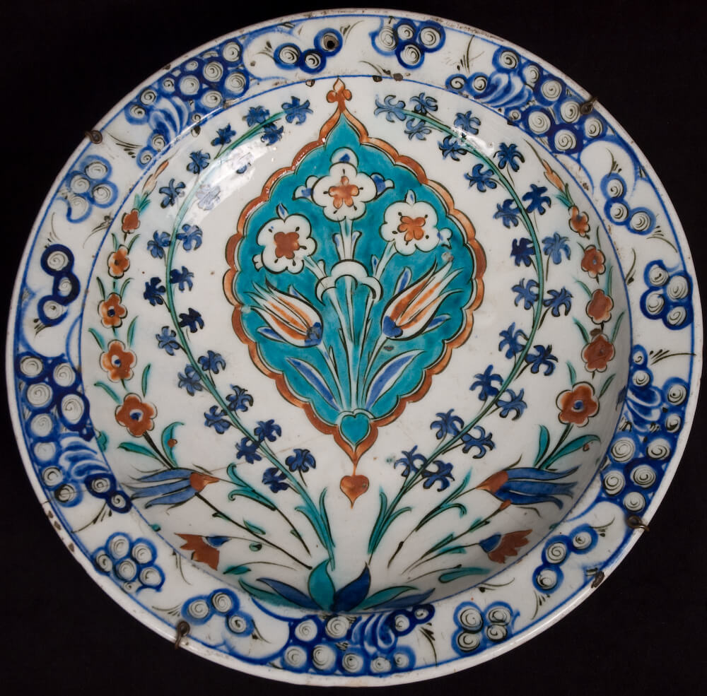 A glazed ceramic plate with blue, teal, and red floral decorations.