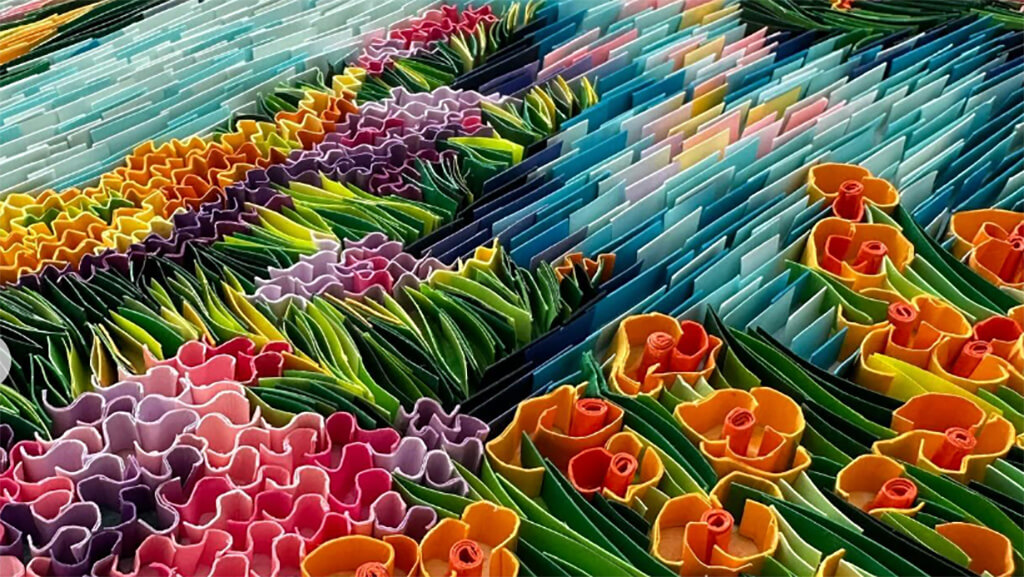 A landscape of flowers next to a river, created by quilled strips of paper.