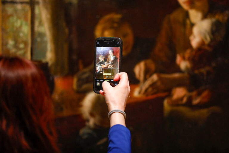 A hand holding up a phone, taking a picture of a painting.
