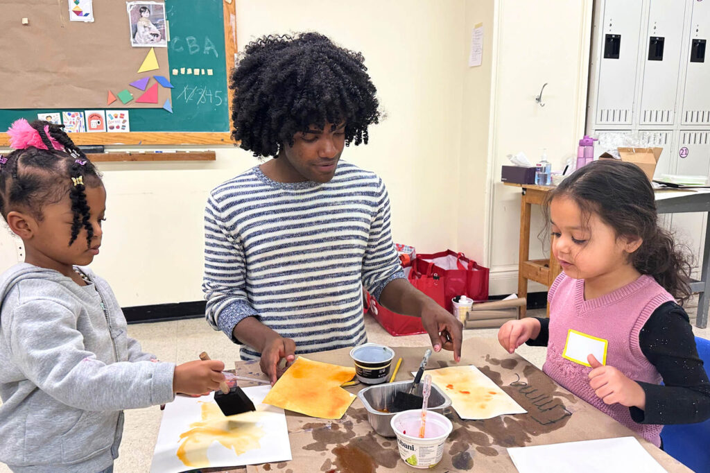 A Creative Workshop instructor helps two Mini campers paint.
