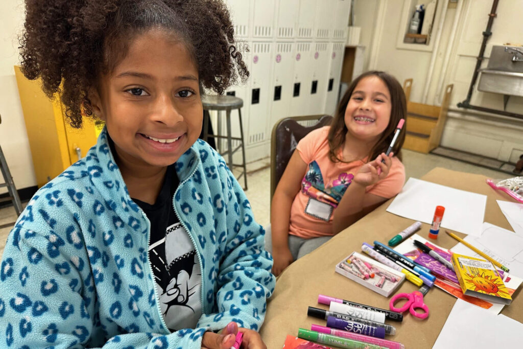 Two girls smiling and having fun while drawing in the Creative Workshop.