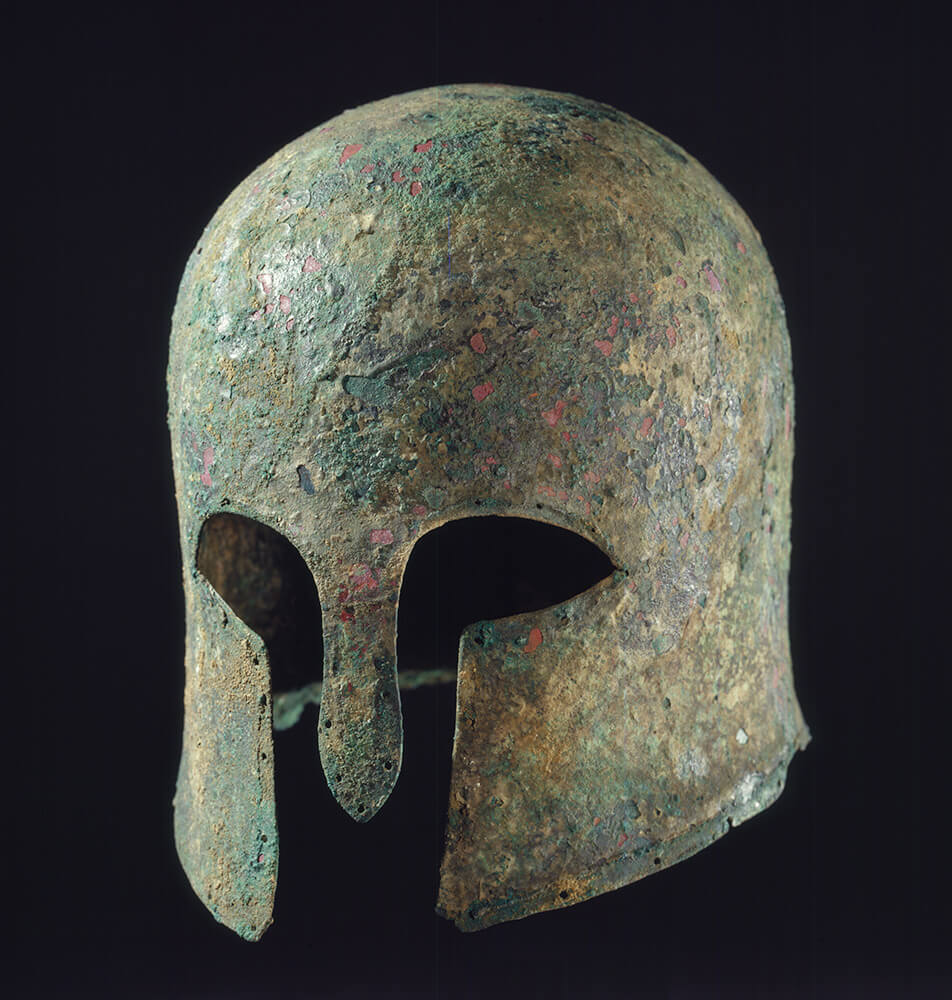 Bronze Greek helmet with a rusted green patina.