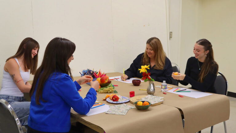 Four women snack, work on art projects, and talk together in the Creative Workshop.