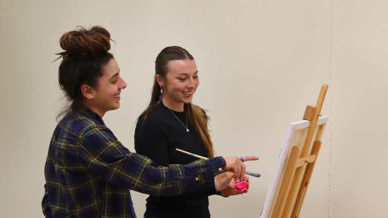 A teacher helps an adult student paint in the Creative Workshop.