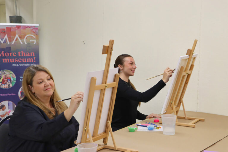 Two adult students painting at easels in the Creative Workshop.