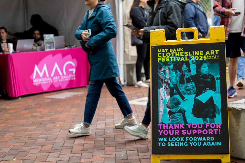 A person walking past a sign reading, "Thank you for your support! We look forward to seeing you again," the MAG Membership tent in the background.