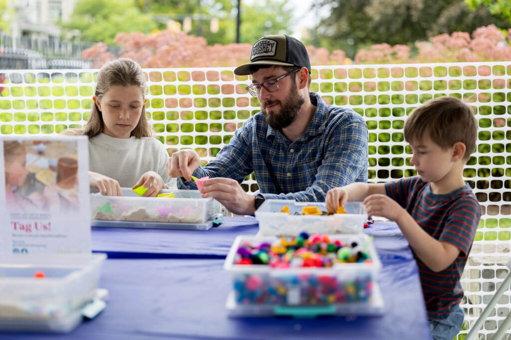 A parent and two kids doing crafts in the 2025 free family fun zone at Clothesline.
