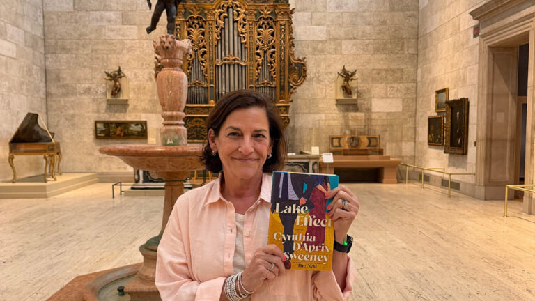 Author Cynthia D'Aprix Sweeney holding her novel in the Fountain Court at MAG.