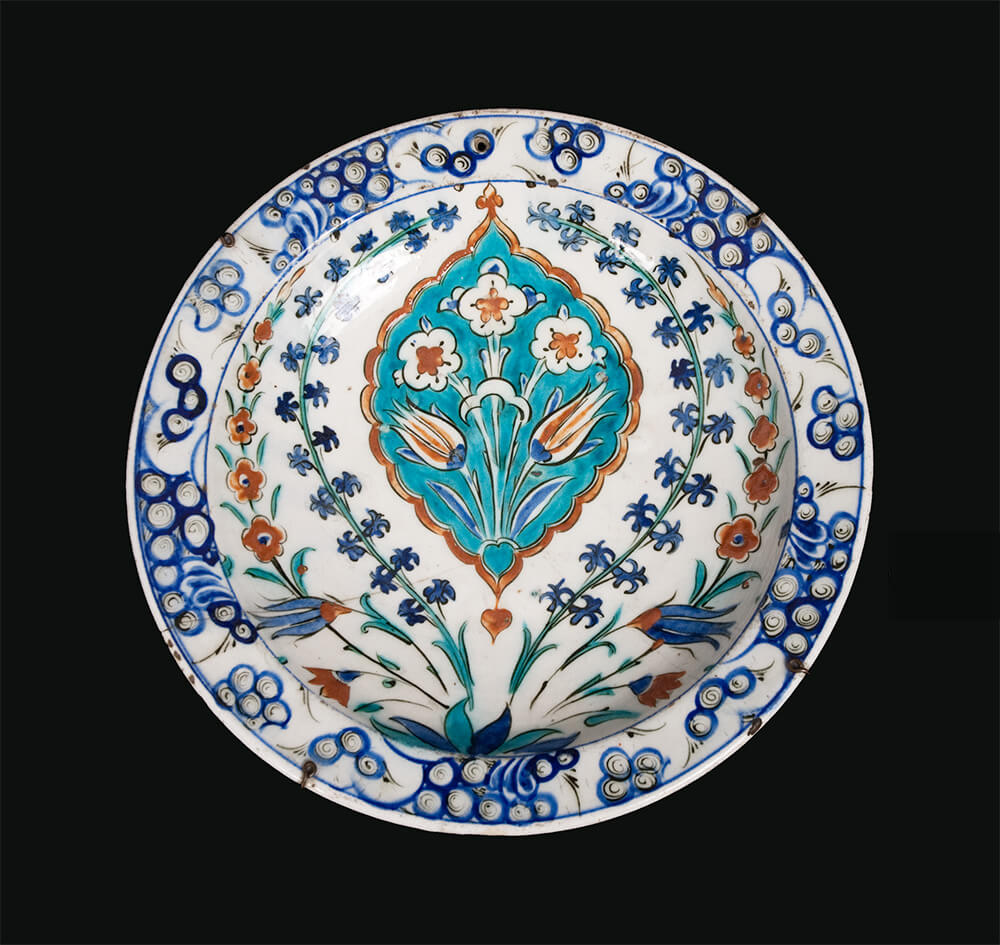 A glazed ceramic plate with blue, teal, and red floral decorations.