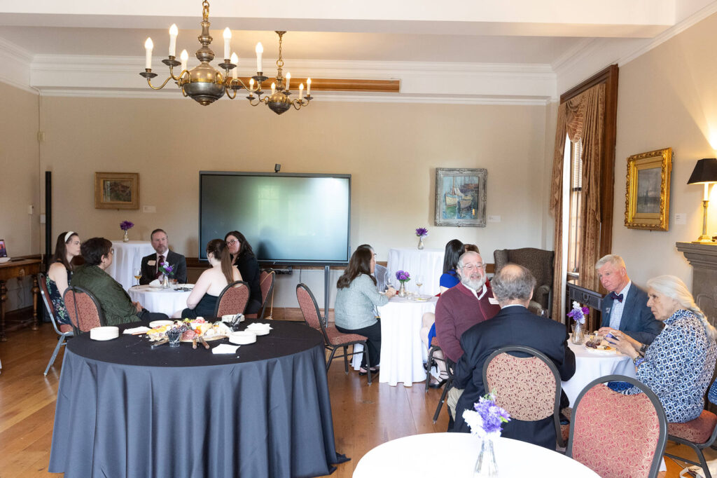 People seated at various small, round tables in the Lynne Lovejoy Parlor.